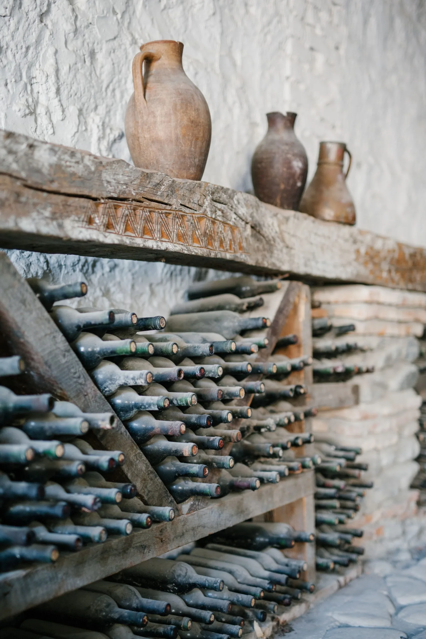 Cave ancienne avec étagères en bois chargées de bouteilles poussiéreuses et cruches en terre