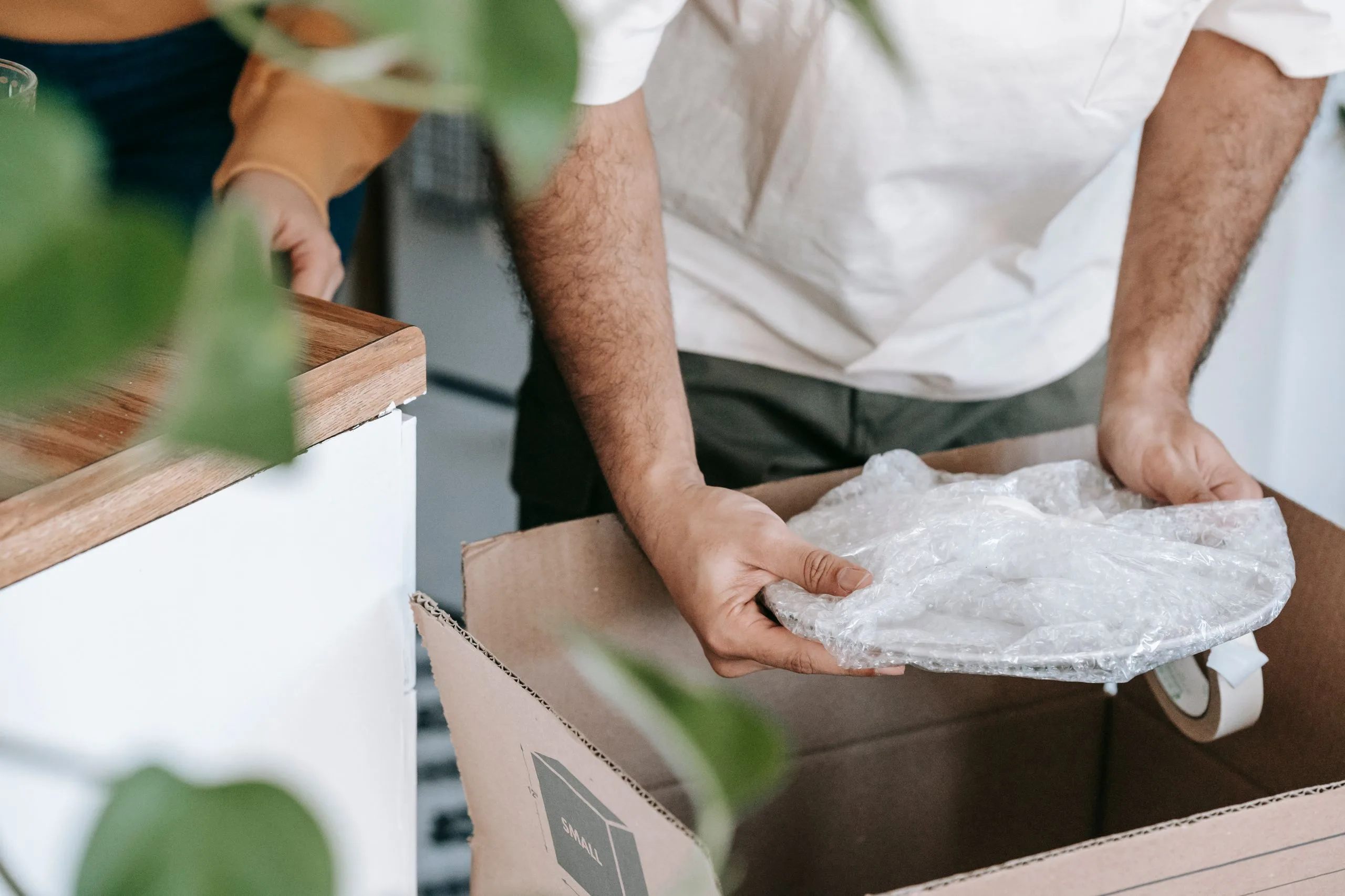 Mains déposant avec précaution une assiette emballée de papier dans une caisse