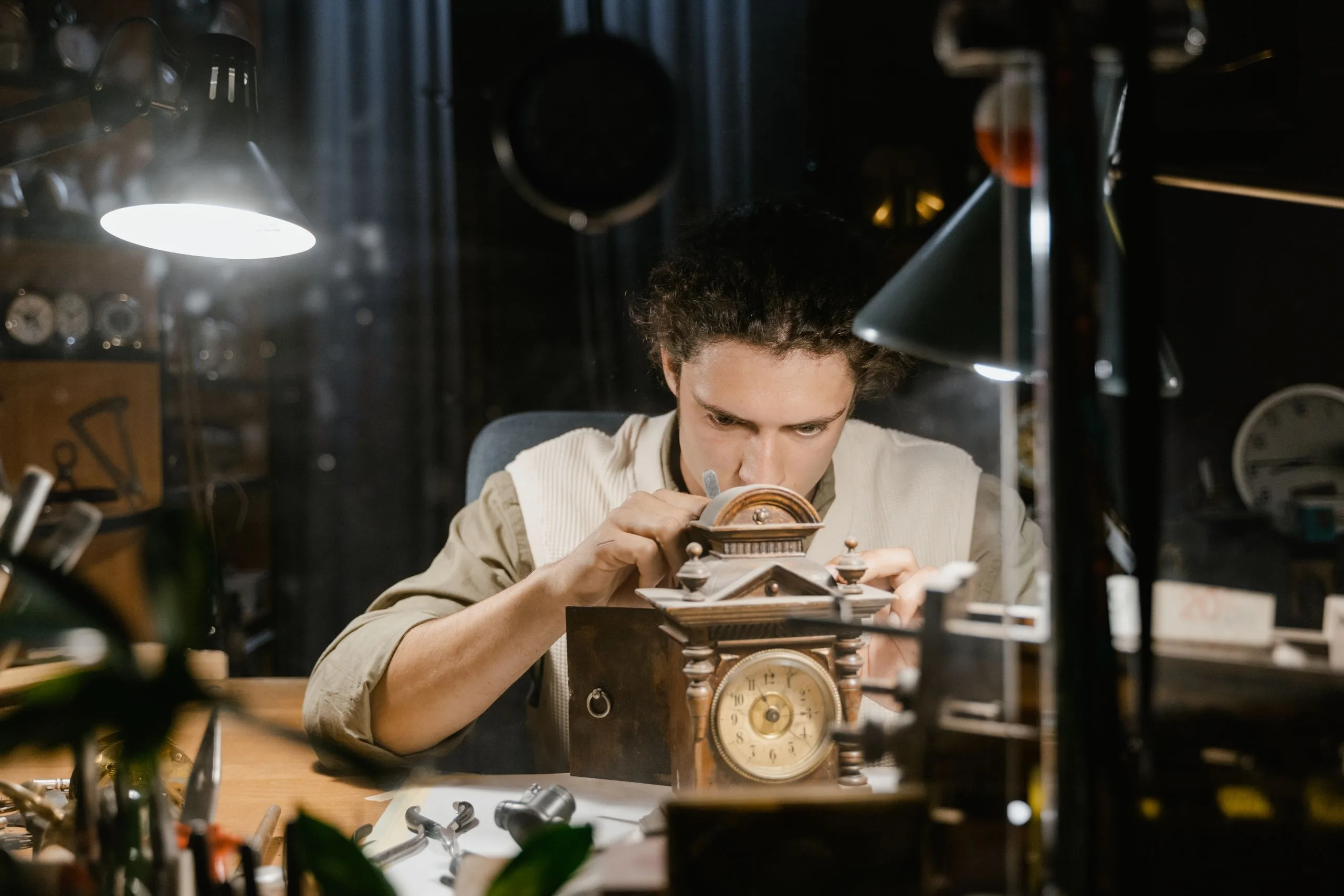 Horloger concentré réparant une horloge ancienne à son établi, sous une lampe chaude