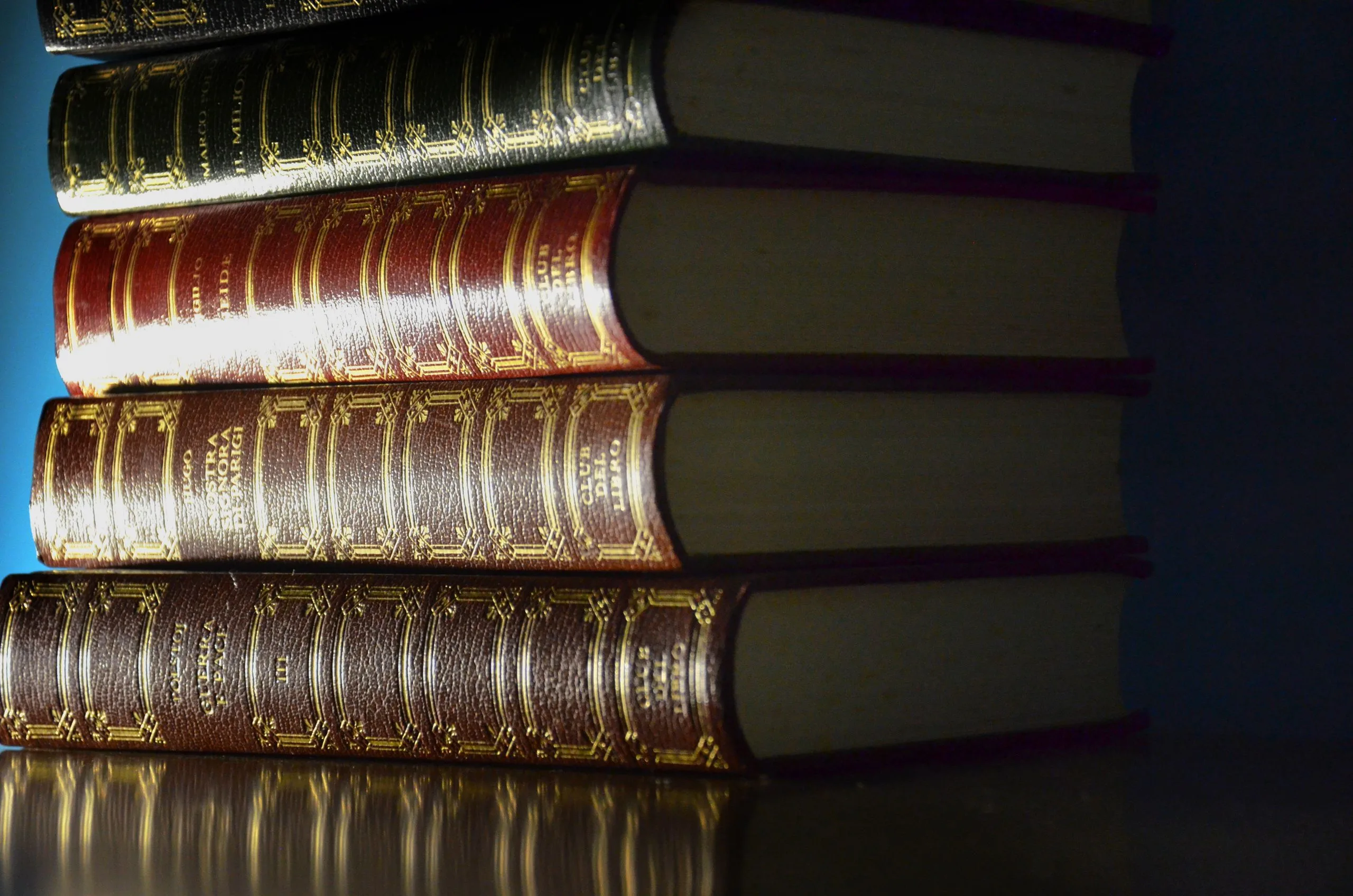 Pile de livres anciens aux reliures de cuir ornées, baignée d'une lumière chaude