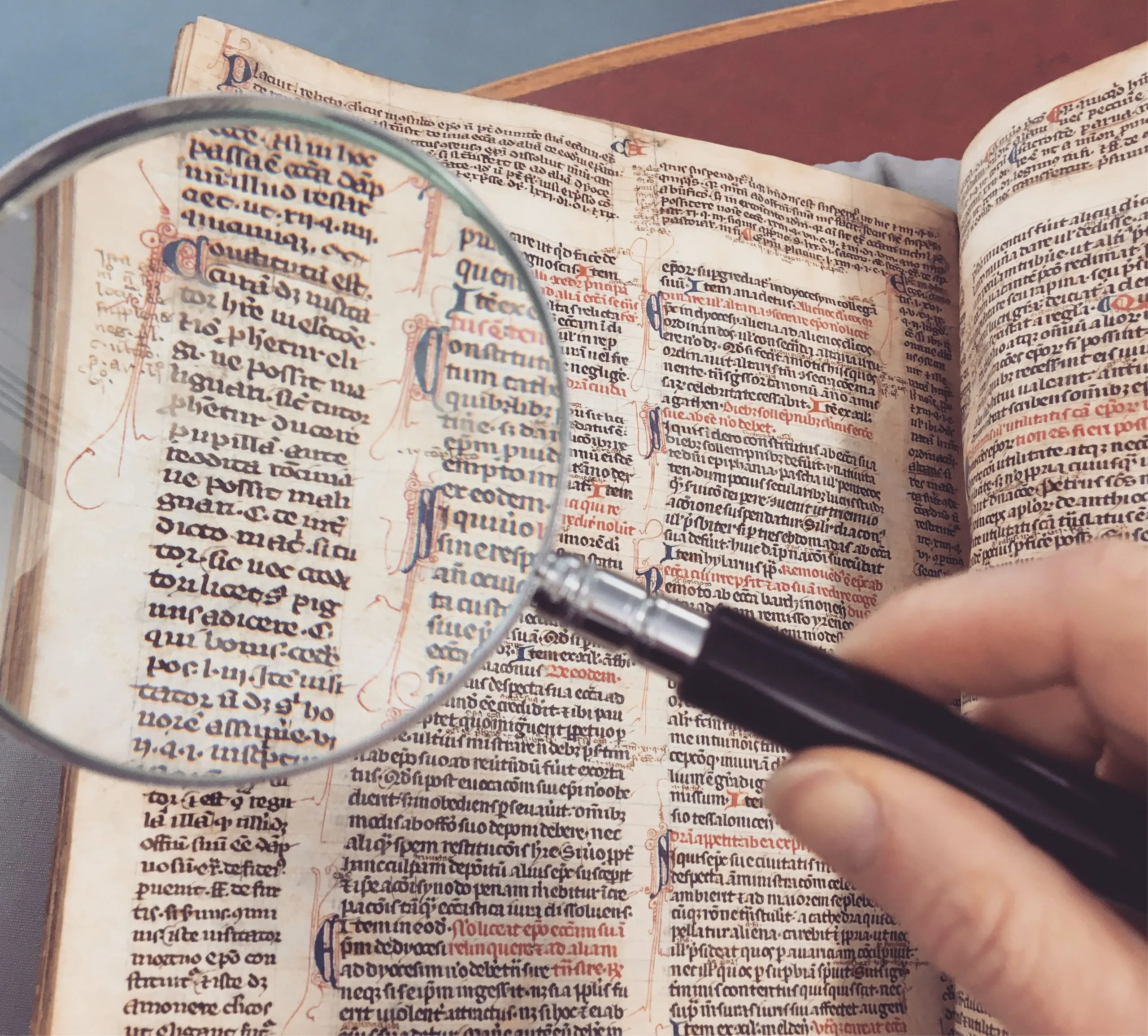 Main tenant une loupe sur la page d'un livre ancien, texte et ornements révélés en détail