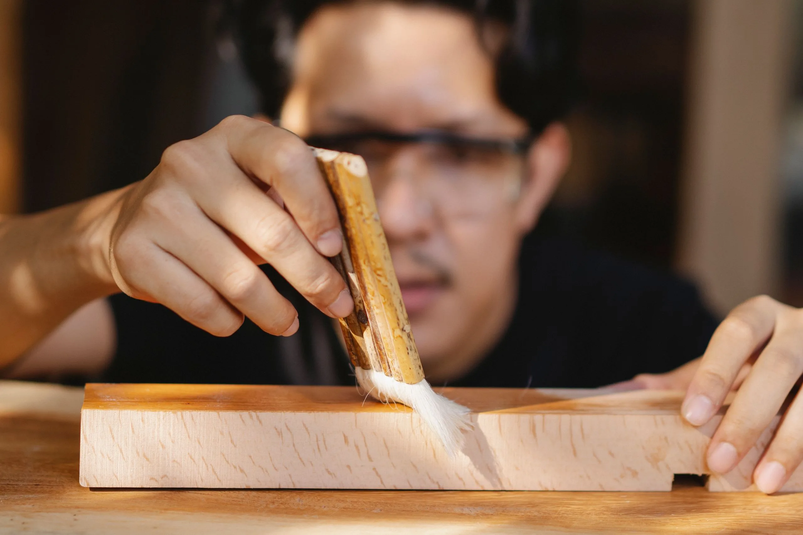Artisan appliquant vernis et cire au pinceau sur une pièce de bois en atelier