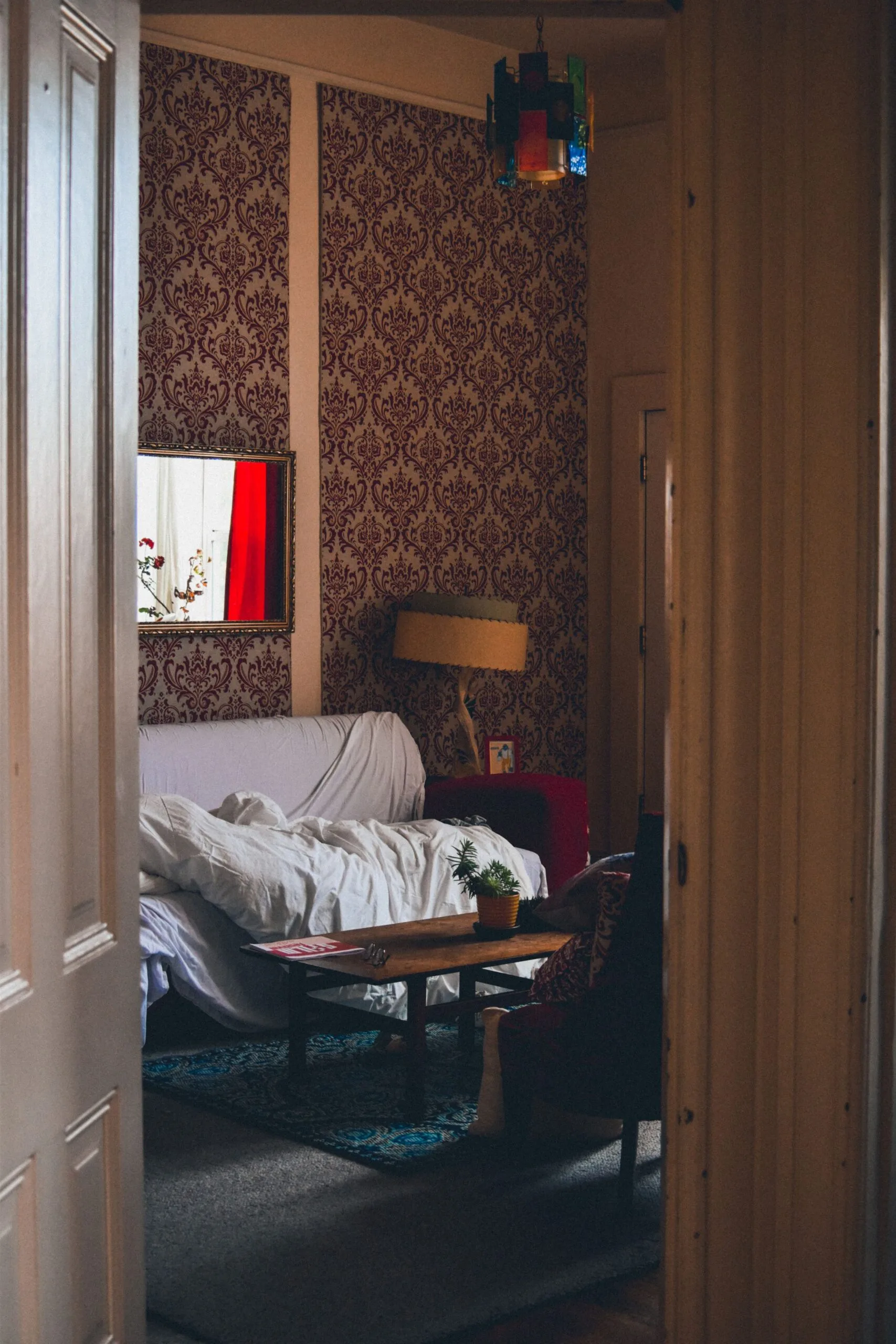 Salon d'une maison ancienne avec papier peint d'époque, mobilier patiné et lumière de fenêtre
